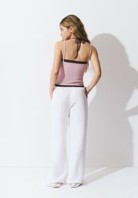 Top sin mangas de canalé rosa con acentos en marrón oscuro, combinado con pantalones de pierna ancha blancos. La parte superior cuenta con tirantes finos y un detalle de lazo en la parte posterior.