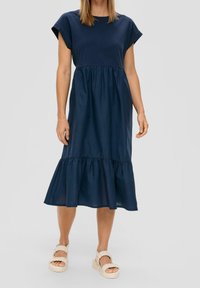 Marineblaues, kurzärmeliges Kleid mit Rundhalsausschnitt, taillierter Taille und gestuftem Rüschensaum. Glattes Baumwollmaterial, knöchellang. Leichte Schuhe.