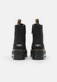 Czarne botki do kostki wykonane z tkaniny z masywną gumową podeszwą, bocznymi zamkami błyskawicznymi i kontrastującymi żółtymi metkami. Posiadają logo na pięcie.