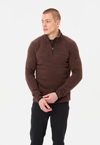 Pullover marrone con zip in un tessuto testurizzato. Presenta un collo alto e polsini neri a contrasto. Sottile, con un dettaglio di cucitura frontale.