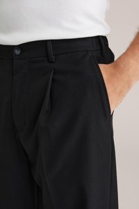 Svarta byxor i slätt tyg, med flat front, sidofickor och en klassisk knappstängning vid midjan.