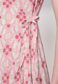 Vestido com padrão floral em tecido leve, apresentando tons de rosa e pêssego, cinchado na cintura com um laço, exibindo textura plissada.