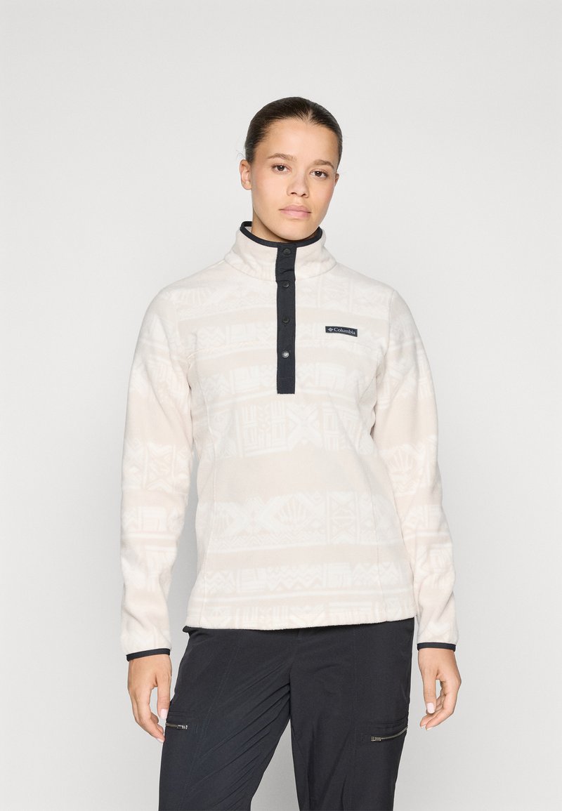 Fleece pullover in lichtbeige met subtiele witte patronen, hoge kraag en marineblauwe accenten. Voorzien van een knoopsluiting aan de voorkant en logo detail.
