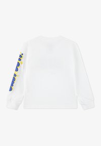 Langärmliges weißes T-Shirt mit einem bunten blauen und gelben Grafikdesign auf dem linken Ärmel. Mit Rundhalsausschnitt und gerippten Bündchen.