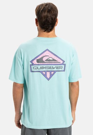 Light blue cotton t-shirt featuring a large graphic in purple and black on the back with the text "QUIKSILVER" and geometric elements.