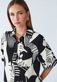 Kurzarmhemd aus Baumwollmischung, mit einem auffälligen schwarz-weißen abstrakten Muster, einem kragenlosen Ausschnitt und einer einzelnen Brusttasche.