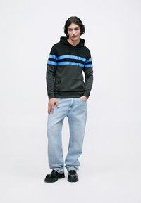 Moletom com capuz com listras horizontais pretas e azuis, combinado com jeans azul claro e sapatos grossos pretos. Tecido suave e casual.