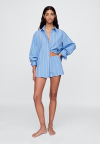 Světlomodrá pruhovaná košile s dlouhými rukávy a výstřihem, doplněná o odpovídající modré šortky. Bavlněný materiál, volný střih.