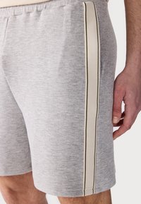 Gray athletic shorts made of soft fabric, featuring a side panel in cream with dark stripes and an elastic waistband for a comfortable fit.