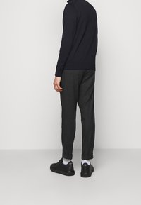 Svart långärmad tröja, grå slim fit-byxor och svarta sneakers. Slät tyg, avslappnad passform och uppvikt fåll på byxorna.