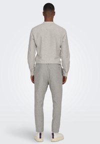 Lichtgrijs shirt met lange mouwen en een ronde hals, gecombineerd met grijze broek met krijtstreepjes en witte schoenen met paarse accenten.