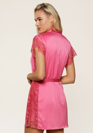 Robe en satin rose avec des manches en dentelle, une taille à nouer et un ourlet court. Texture lisse, couleur vive et détails en dentelle complexes sur les côtés.