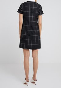 Svart rutig klänning med korta ärmar, vit krage och figurnära silhuett. Strukturerat material med framträdande vit rutmönster.