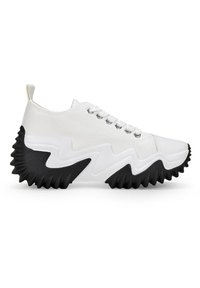 Sneaker di tela bianca con suola in gomma nera, caratterizzata da un motivo a zigzag, punta rotonda, design con lacci e un'etichetta sul tallone.