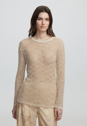 Beige Strickpullover mit einem strukturierten Muster, langen Ärmeln und einem runden Ausschnitt. Kombiniert mit hellen, gemusterten Hosen.