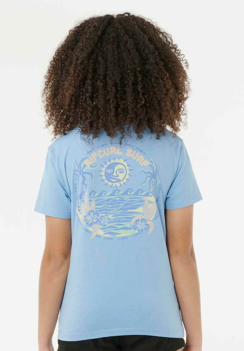Persona con cabello rizado que lleva una camiseta azul claro con un diseño de sol, olas, flores y el texto "RIP CURL SURF" en la parte de atrás.