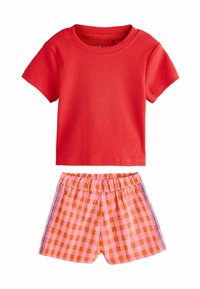 Camiseta roja de manga corta con textura acanalada combinada con pantalones cortos de cuadros en naranja y rosa que presentan una cintura con volantes y acentos estampados laterales.