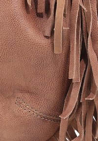 Bruine leren tas met een ge textured oppervlakte, voorzien van lange franjes en een gestikte zak. De vorm is zacht en slonzig.