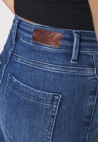 Jeans de ganga azuis com um patch de couro rotulado "ONLY" na cinta, com um bolso traseiro padrão e detalhes de costura discretos.