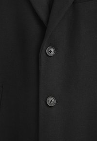 Svart ullblandad kappa med slagkrage, texturerad tyg och två framträdande svarta knappar med präglad "Polo Club"-logotyp.