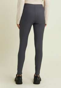 Leggings grigi in tessuto elasticizzato, con una superficie liscia e una vita alta. Abbinati a scarpe da ginnastica nere.