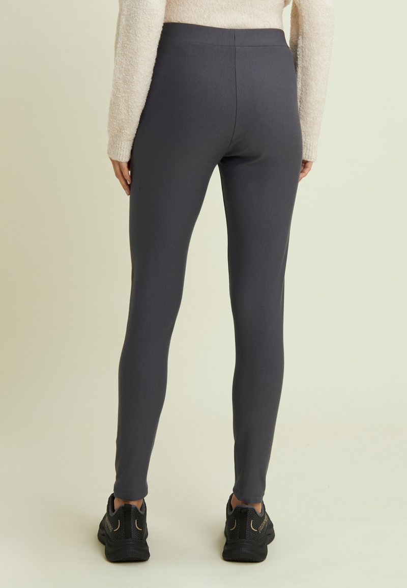 Leggings grigi in tessuto elasticizzato, con una superficie liscia e una vita alta. Abbinati a scarpe da ginnastica nere.