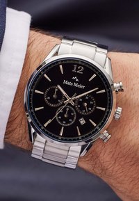 Silver stainless steel watch with a black dial, three sub-dials, gold hour markers, and a date display. Features a metal link bracelet.