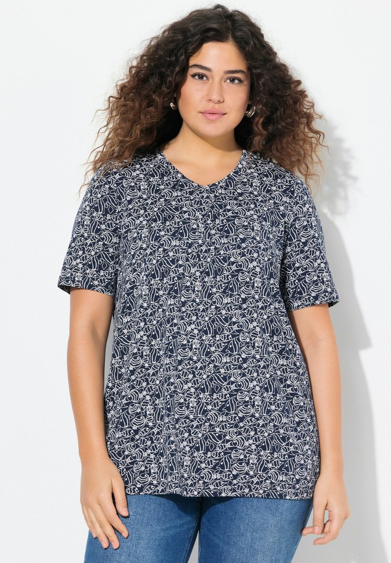 T-shirt a maniche corte blu navy con scollo a V, caratterizzato da un motivo floreale bianco. Tessuto morbido con vestibilità comoda, indossato con jeans blu.