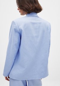 Ljusblå linnesakko med skräddarsydd passform, breda slag och en mjuk textur. Har en ren, minimalistisk design på baksidan.