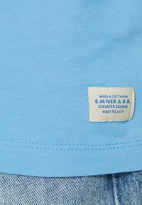 Svetlomodré bavlnené tričko s prišitým lemom. Obsahuje smotanovú etiketu s modrým textom "S.OLIVER A.R.R." a pokyny na údržbu.