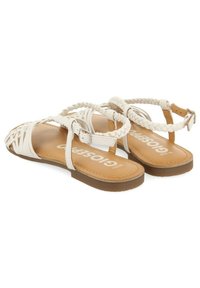 Sandalias trenzadas blancas con suelas planas, una correa ajustable en el tobillo y una plantilla texturizada. Diseño ligero adecuado para un uso casual.
