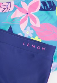 Kwiatowy górny część stroju kąpielowego w różowe i niebieskie wzory, w połączeniu z jednolitymi granatowymi dolnymi częściami z różowym logo "LEMON" na pasku.