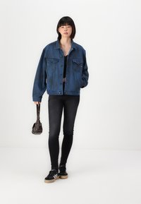 Τζάκετ από τζιν σε σκούρο μπλε χρώμα με χαλαρή εφαρμογή, δύο τσέπες στο στήθος και κλείσιμο με κουμπί. Συνδυασμένο με μαύρο εφαρμοστό τζιν και μαύρα αθλητικά παπούτσια.