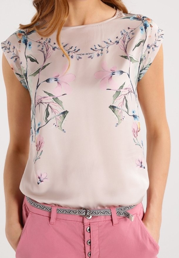 Blouse rose clair à manches courtes avec imprimé floral aux couleurs pastel. Texture lisse avec un col rond, associée à un pantalon rose et une ceinture à motifs.
