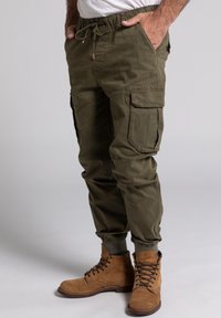 Olivengrüne Cargo-Hose mit elastischem Bund, Kordelzug und seitlichen Taschen. Kombiniert mit braunen Schnürstiefeln.