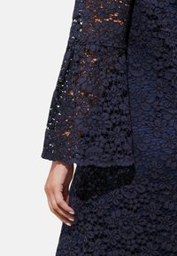 Navy blauwe kanten jurk met een bloemenpatroon, driekwart mouwen en een gegolfde zoom. Gladde textuur met doorschijnende delen.