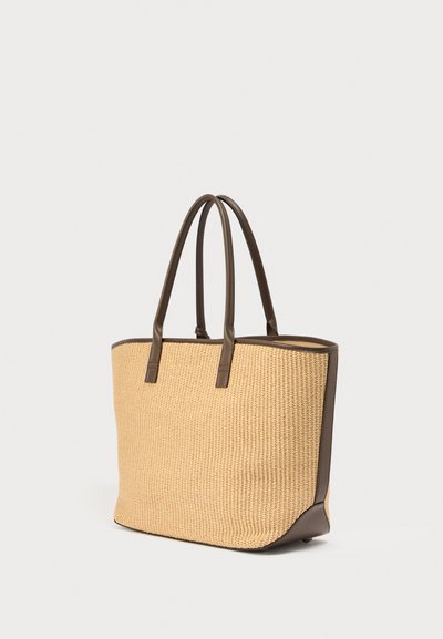 Sac fourre-tout tissé beige avec poignées, garniture et base en cuir marron foncé, debout sur un fond blanc.