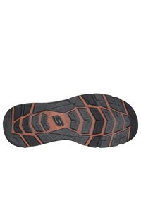 Suela de goma negra con patrón de tracción hexagonal, que presenta acentos en color naranja. Incluye la marca "STADY GRIP" en el centro.