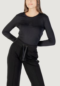 Maglietta nera a maniche lunghe con colletto tondo e dettaglio logo scintillante sul petto, abbinata a pantaloni jogger neri con vita regolabile.