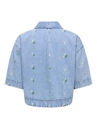 Veste en denim bleu clair à manches courtes avec de petites broderies de marguerites blanches dispersées sur le tissu.