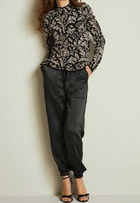Maglia a maniche lunghe nera e beige con motivi floreali ornamentali, abbinata a pantaloni neri lisci e sandali neri con cinturini.