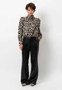 Geknoopte blouse met een beige en zwart zebra patroon, gecombineerd met zwart leren broek met hoge taille en gestreepte hakken.