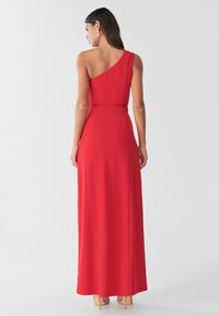 Vestido maxi rojo de un solo hombro con tela suave, cuerpo ajustado, acento en la cintura y falda fluida que llega hasta la mitad de la pantorrilla, combinado con tacones nude.