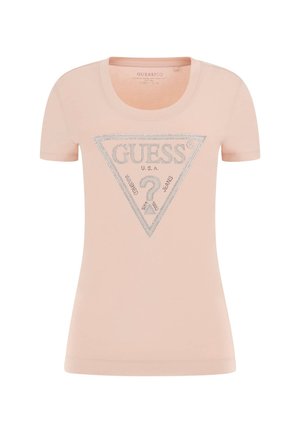 Lyserød t-shirt med korte ærmer med en sølvglitrende trekantet Guess-logo og teksten "U.S.A. Guess Jeans" på fronten.