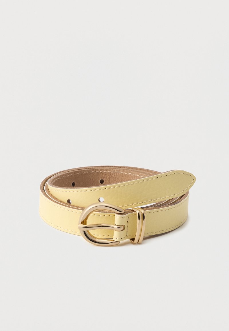 Ceinture en cuir jaune clair roulée avec une boucle arrondie dorée et plusieurs trous de réglage sur un fond blanc uni.