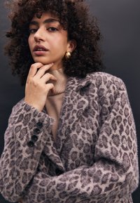 Faux-Fur-Blazer in Helllila mit Leopardenmuster; verfügt über einen abgestuften Kragen, vier schwarze Knöpfe an den Ärmeln und eine weiche Textur.