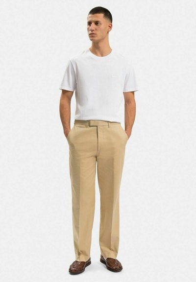 Vit bomull t-shirt, beige dressade byxor och bruna mönstrade loafers. T-shirten har en rund halsringning; byxorna har rak skärning och bälteshällor.