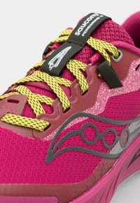 Zapatilla de running Saucony con un upper de malla rosa, cordones amarillos, acentos de goma y un logo lateral texturizado y brillante. Diseño de perfil bajo con amortiguación.