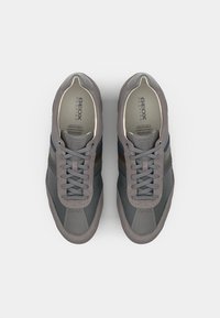 Zapatillas Geox grises con paneles de malla, franjas azules y marrones, y suelas texturizadas. Presentan cordones y un forro interior transpirable.