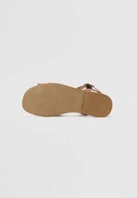 Flat sandal såle med en teksturert brun gummibase, med en lett bue og pregete detaljer, designet for komfort og grep.
